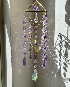 a wall hanging with purple and clear beads on it's side, next to a window