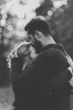 black and white photo of a couple embracing each other in front of some trees with the sun shining on them