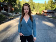 a woman standing on the side of a road in front of some houses and trees