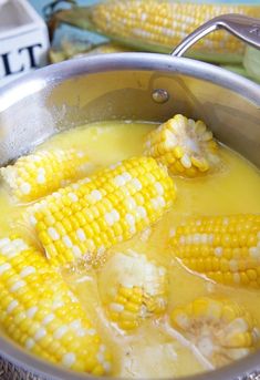 corn on the cob being cooked in a pot with broth and cheese sauce