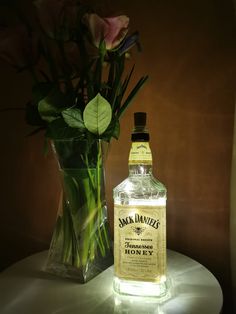 a glass vase with flowers in it next to a bottle of rum and some water