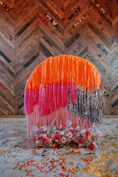 an orange and pink cake with flowers on the top is surrounded by confetti