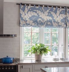 a potted plant sitting on top of a kitchen counter next to a window covered in blue and white damask