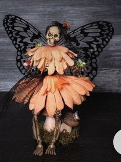 a statue of a skeleton sitting on top of an orange flower with a butterfly wings