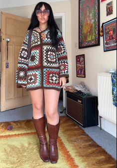 a woman standing in a living room wearing boots and a crocheted sweater over her body