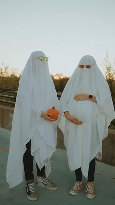 two people dressed in white are holding pumpkins