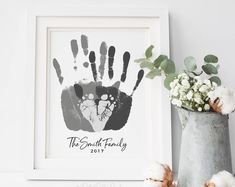 a white frame holding a black and grey hand print with flowers in the vase next to it