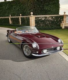 a red sports car is parked on the side of the road in front of some hedges