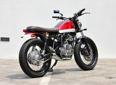 a red and white motorcycle is parked in a parking lot next to a gray wall