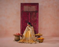 a woman in a yellow and gold dress sitting on a table with bowls of flowers