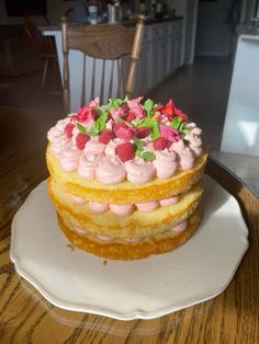 a three layer cake with pink frosting and strawberries on top sitting on a white plate