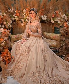 a woman in a wedding dress sitting on a couch with flowers and plants around her