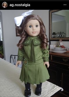 a doll with long hair wearing a green dress and black shoes on top of a bed