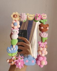 a hand holding a cell phone in front of a mirror with flowers and bears on it