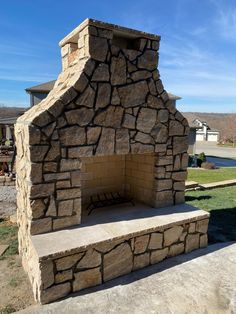 DIY Outdoor Fireplace in Backyard with veneer stucco flagstone lighting. Angled chimney and chimney cap installed. Grass behind fireplace with large stamped concrete patio. 2023 Landscape, Outside Fireplace