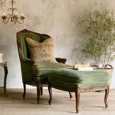 a green chair sitting next to a table with a vase on it and a lamp hanging from the ceiling