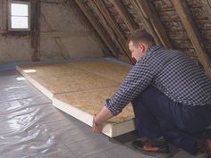 a man kneeling down on top of a mattress in an attic with exposed rafters