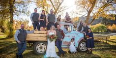 a bride and groom posing with their wedding party in the back of an old truck