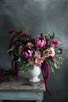 a white vase filled with lots of flowers on top of a wooden table next to a gray wall