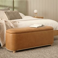 a bed with a brown foot stool next to it and a book on the end table