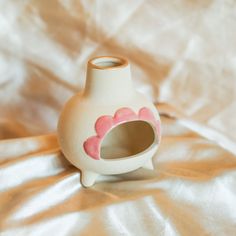 a small white vase with pink hearts painted on the side and inside is sitting on a shiny surface