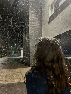 a woman standing in front of a building with snow falling all over her and looking at the street