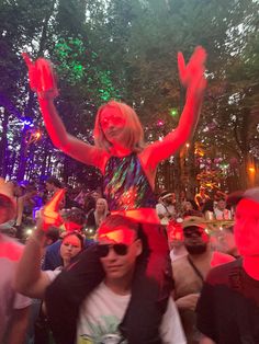 a woman with her arms up in the air at a music festival, surrounded by other people