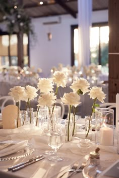 white flowers are arranged in vases on the table at a formal dinnereone