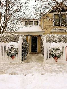 a house covered in snow next to a white picket fence with wreaths on it