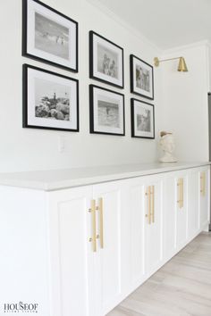 a kitchen with white cabinets and framed pictures on the wall above it, along with gold handles