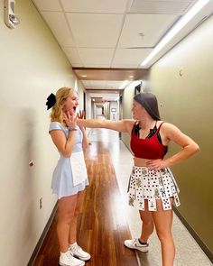 two young women standing in a hallway pointing at each other