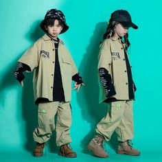 two young children dressed in khaki clothing and hats, standing against a green background