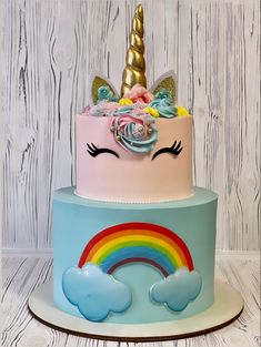 a multi layer cake with a rainbow and unicorn face on top