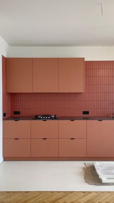 an empty kitchen with wooden floors and pink cabinets on the wall, next to a stove top oven