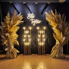 the entrance to an event decorated with tall, feathery plants and lights in front of a black wall