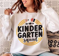 a woman sitting on a couch wearing a white shirt with the words kinder garter squad printed on it