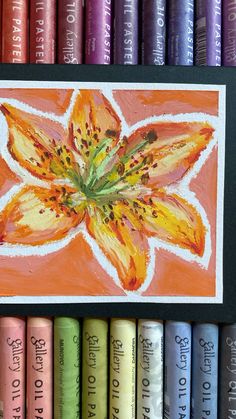 an orange flower painted on a card surrounded by colored crayons