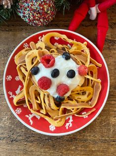 a red plate topped with pasta covered in cream and berries next to a elf's head