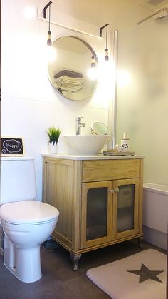 a white toilet sitting next to a wooden cabinet in a bathroom under a round mirror