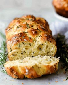 a loaf of bread with cheese and rosemary sprigs on it, cut in half