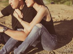 a young man and woman sitting on the ground next to each other with their arms around each other