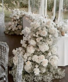 white flowers and greenery are arranged on the table for an elegant wedding reception in front of large glass windows