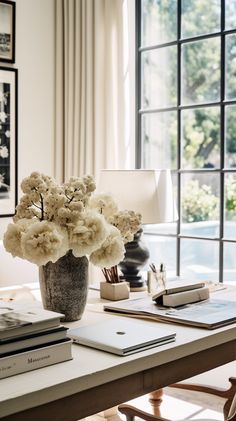 a vase with white flowers sitting on top of a table next to a lamp and books