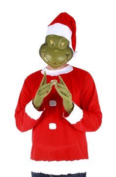 a man in a red shirt and green frog mask standing with his hands together while wearing a santa hat