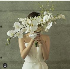 a woman in a white dress holding a bouquet of flowers over her face with both hands