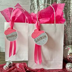 two paper bags with pink bows and name tags on them, sitting on a table