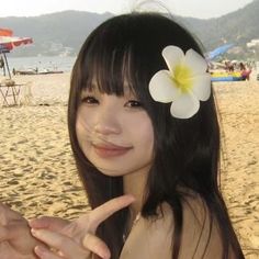 a woman with a flower in her hair making the peace sign at the beach while wearing a bathing suit