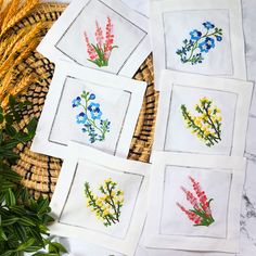 four embroidered napkins with flowers on them sitting next to some grass and plants in the background