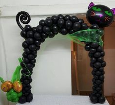 an arch made out of black balloons with a cat on top and a green plant in the middle