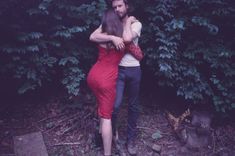 a woman in a red dress is hugging a man